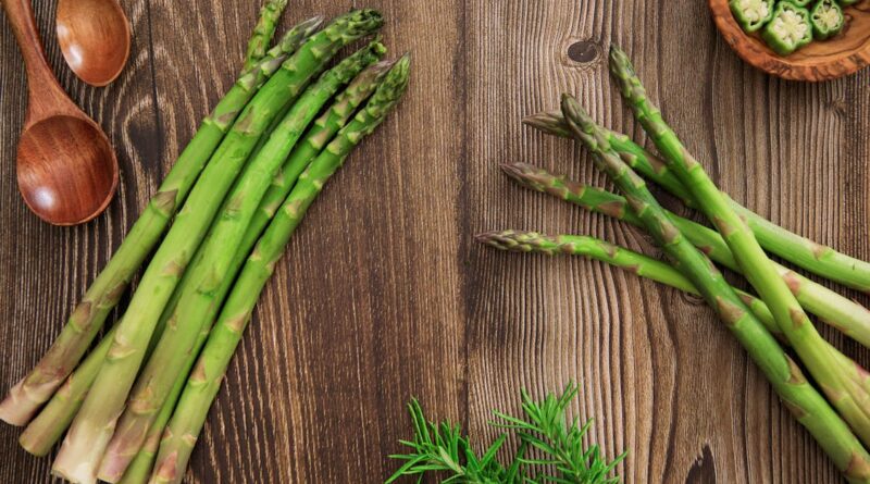 Fresh British asparagus spears arranged on a rustic wooden table with herbs and wooden spoons