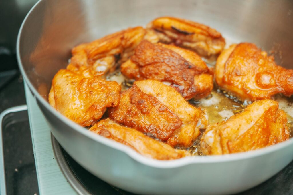 Chicken thigh recipes UK: bone-in chicken thighs frying skin-side down in a cast-iron pan.