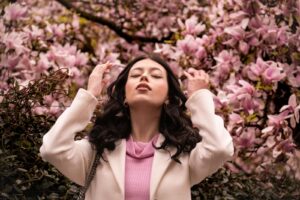 Woman stands among blossoming trees on a sunny spring day, illustrating the link between pollen season and hay fever skin.