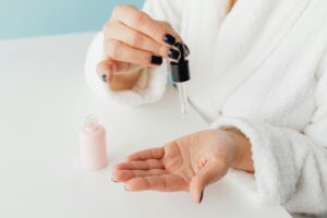 A person in a white dressing gown dispensing hydrating serum from a glass dropper onto the palm of their hand.