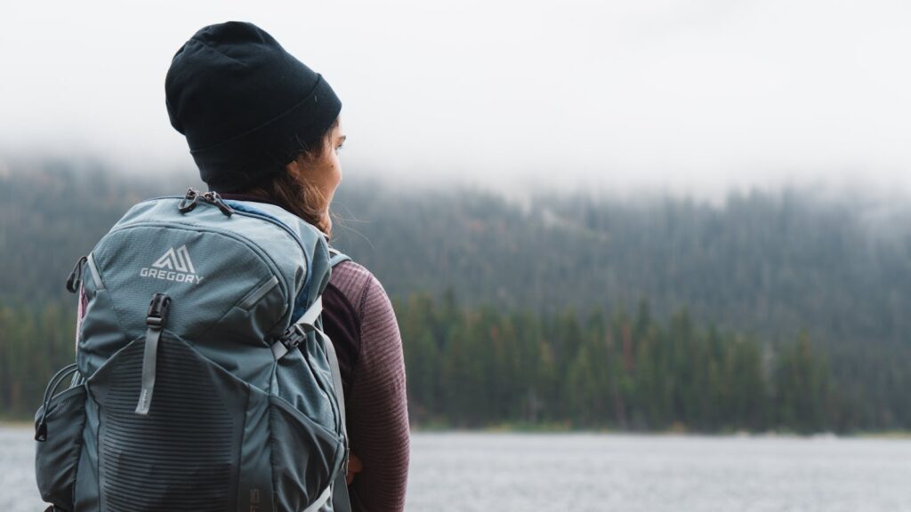 A woman with a backpack pauses by a misty UK lake on a rucking for women UK walk