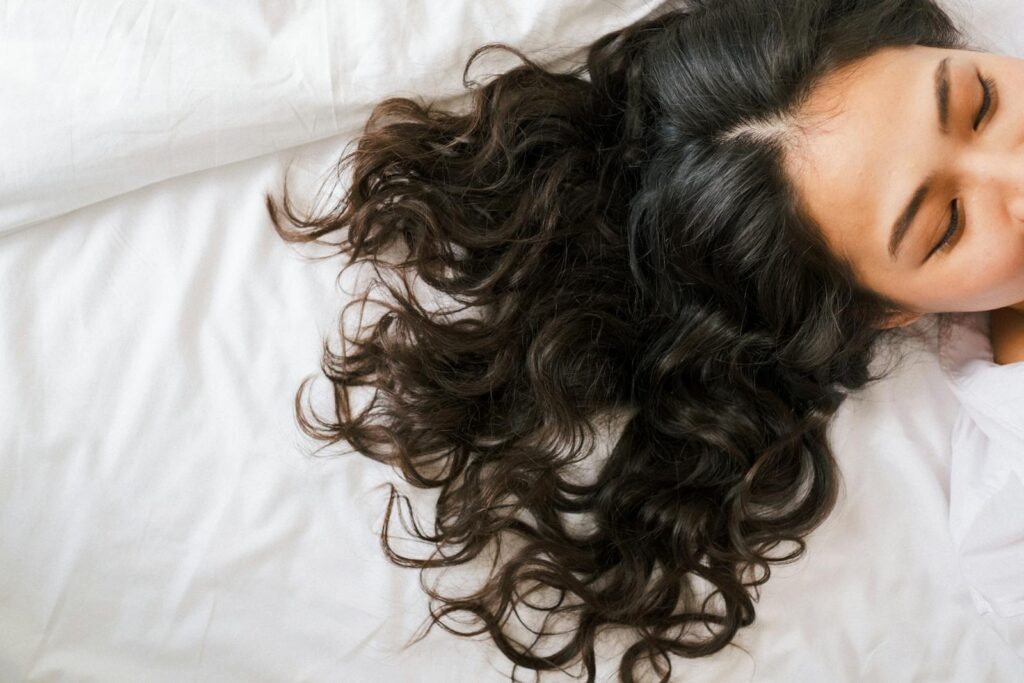 Woman with long dark hair fanned across a pillow, illustrating spring hair shedding UK women notice in April