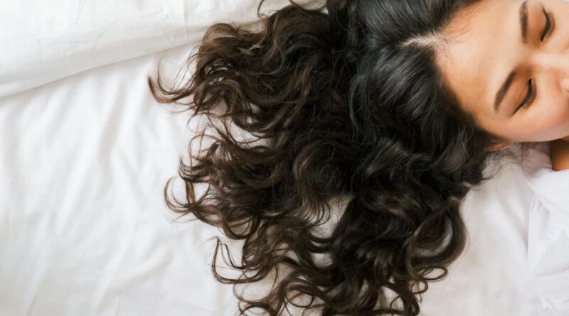 Woman with long dark hair fanned across a pillow, illustrating spring hair shedding UK women notice in April