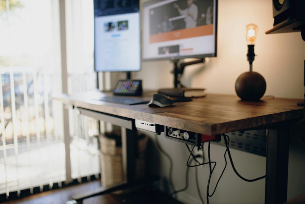 Wooden standing desk converter setup in a UK home office in 2026 with dual monitors and a warm desk lamp.