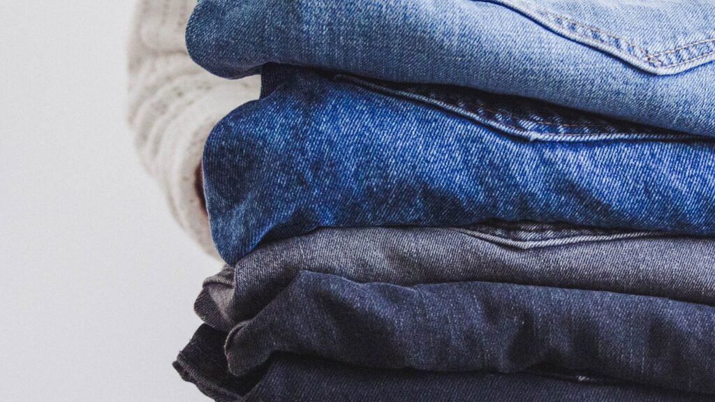 A stack of folded barrel jeans in indigo, mid-blue, black and grey washes - the UK high street's defining spring 2026 denim silhouette.
