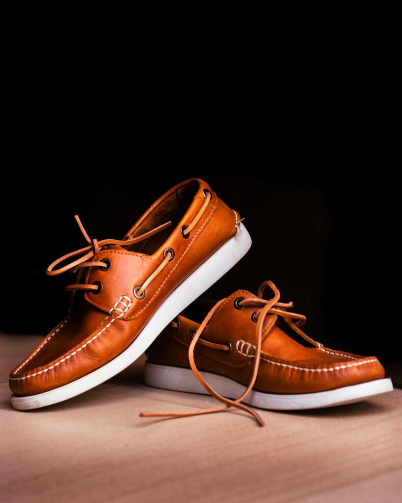 Tan leather boat shoes UK 2026 trend, photographed on a wooden surface against a dark backdrop