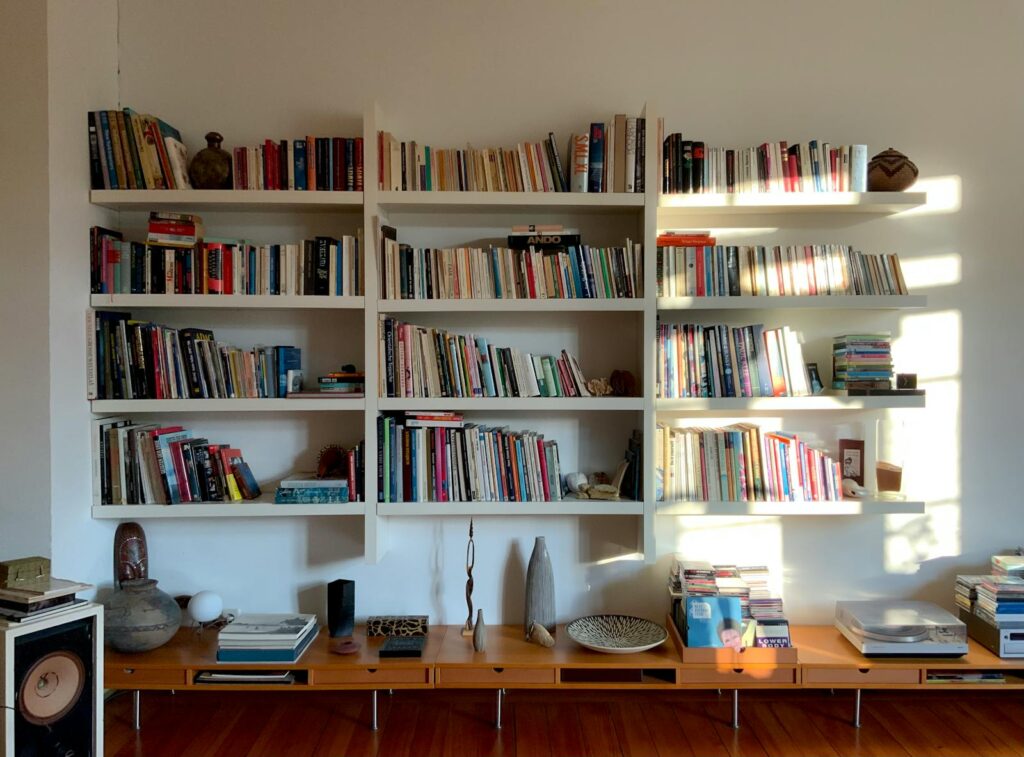 A floor-to-ceiling bookshelf wealth UK style living room with mixed paperbacks, hardbacks, art books and ceramics on a mid-century credenza.