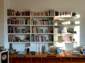 A floor-to-ceiling bookshelf wealth UK style living room with mixed paperbacks, hardbacks, art books and ceramics on a mid-century credenza.