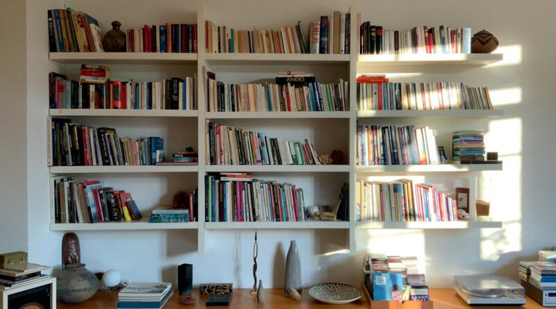 A floor-to-ceiling bookshelf wealth UK style living room with mixed paperbacks, hardbacks, art books and ceramics on a mid-century credenza.