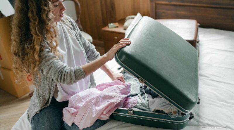 Woman packing a green suitcase with clothes for a city break capsule wardrobe UK trip