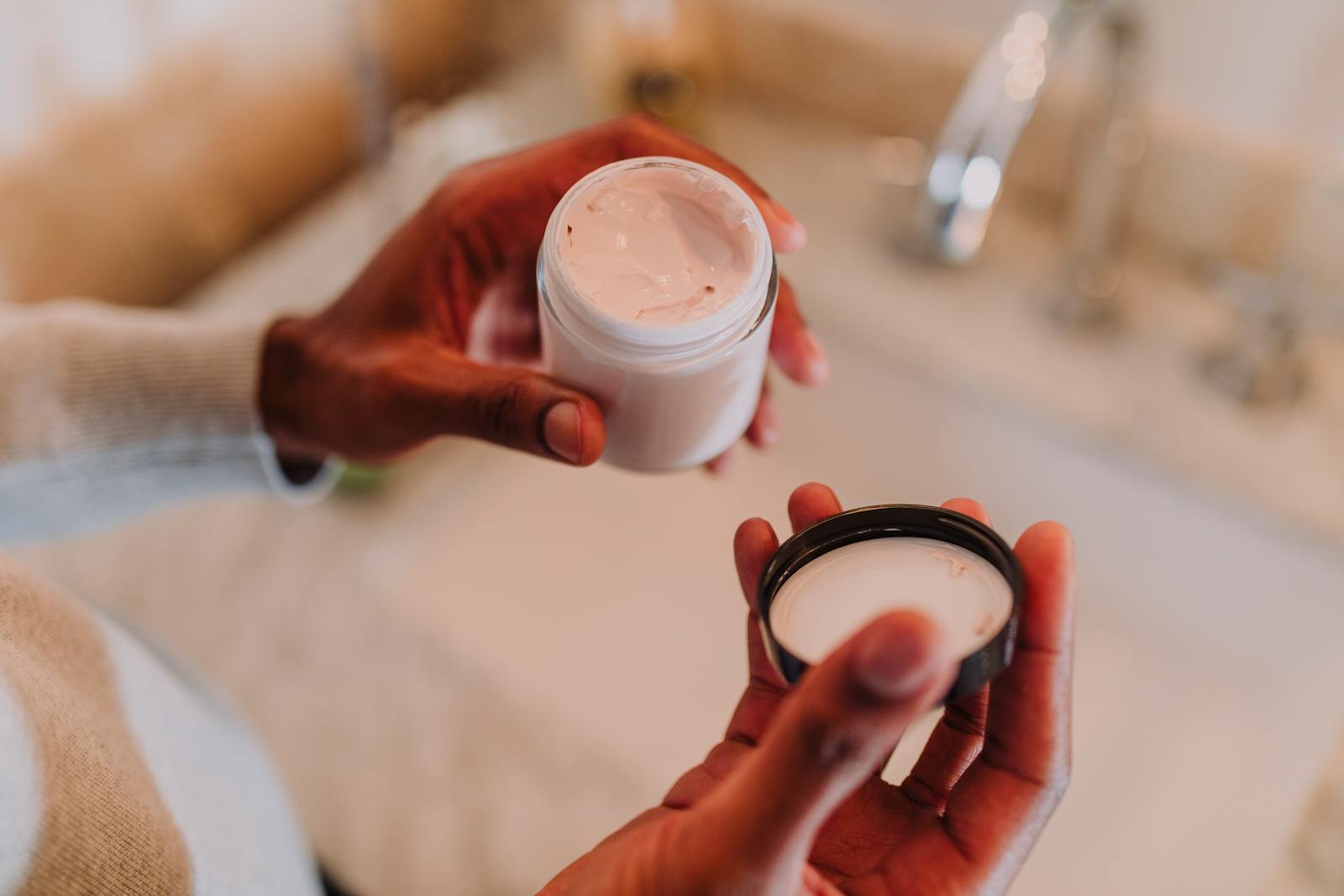Hands holding an open jar of thick balm-style moisturiser