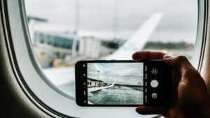 A UK traveller holding a smartphone with a plane wing in view, illustrating eSIM UK travel 2026 connectivity for European holidays.