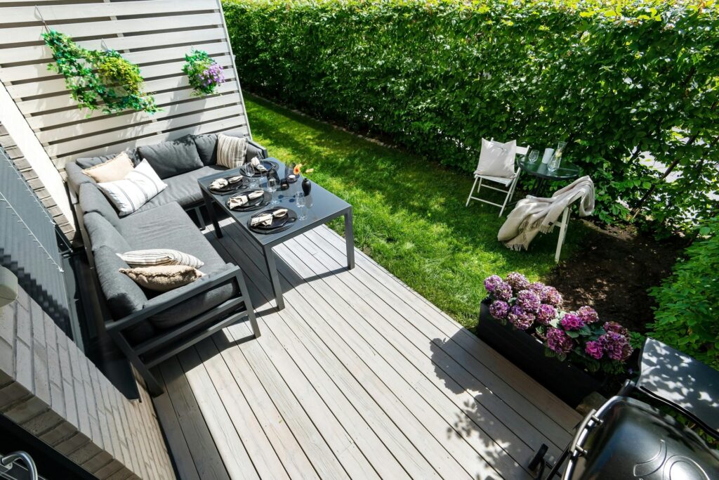 Modular charcoal garden sofa UK on decking with hydrangeas, illustrating the outdoor lounge replacing the traditional patio set