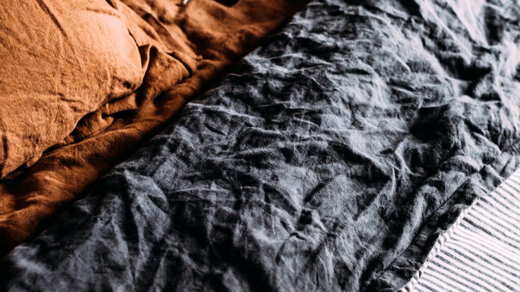 Rumpled rust and charcoal linen bedding showing the texture and crinkle that makes linen bedding UK shoppers love it for warm summer nights.