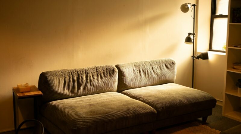 A warmly lit living room sofa under a single floor lamp, illustrating the no big light trend in UK homes in 2026.