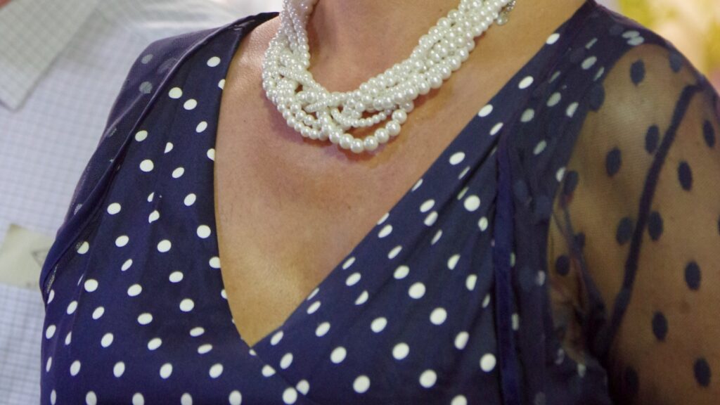 A woman wearing a navy polka dots dress with white spots and a pearl necklace at a UK fashion event.