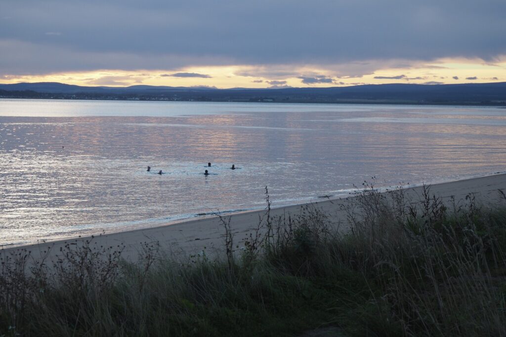 Wild swimmers entering the sea at Rosemarkie Beach, an example of the UK wild swimming 2026 weekend habit