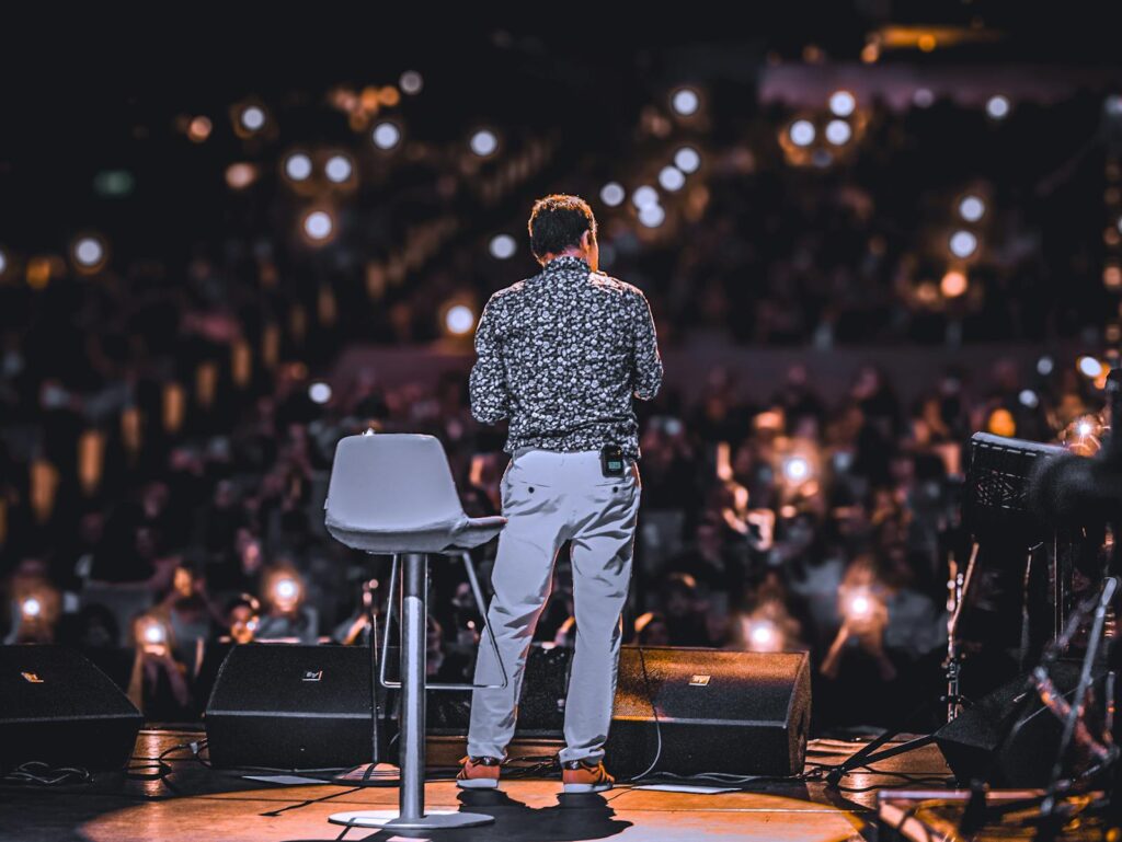 A stand-up comedian on stage facing the audience under stage lights, illustrating the British stand-up on Netflix UK boom.