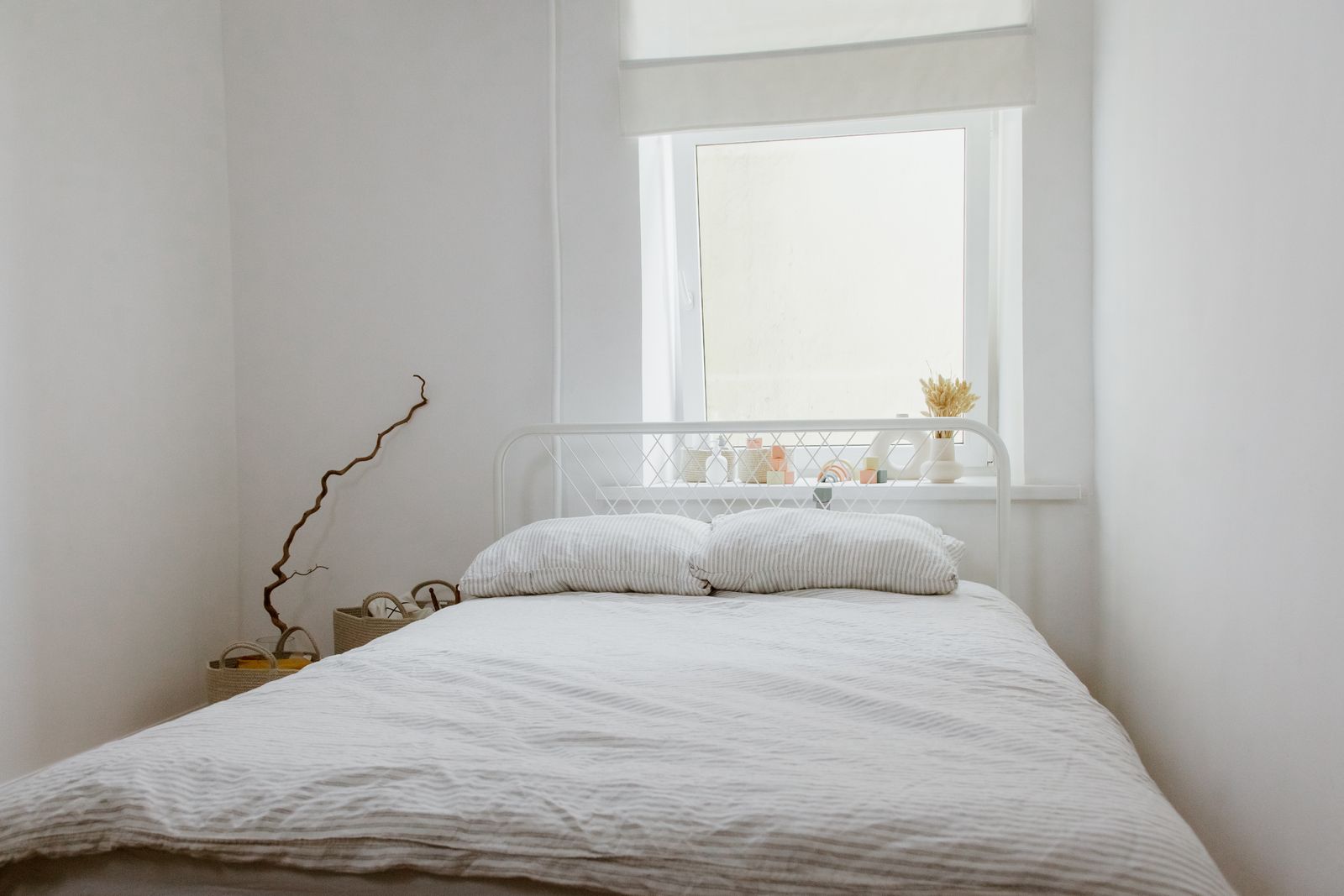 A bright, airy bedroom with light cotton bedding and a window kept shaded through the day