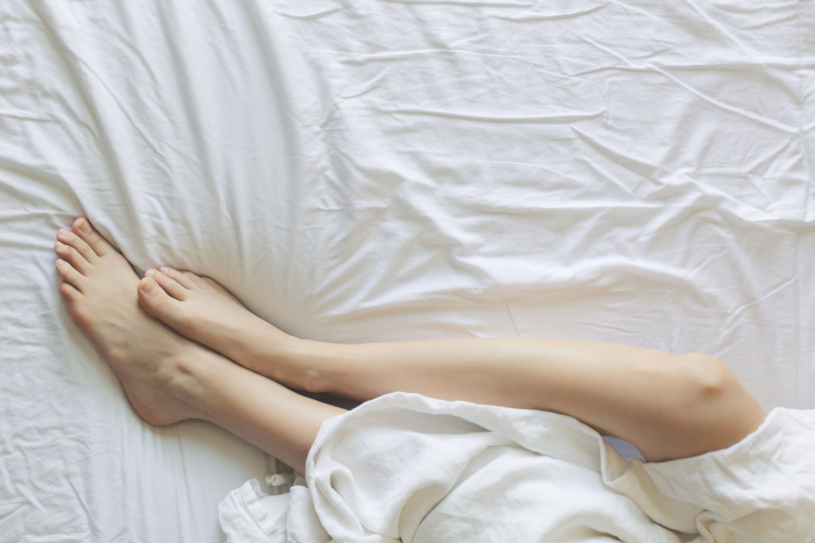 Bare legs on top of white cotton sheets with the duvet kicked off on a hot night