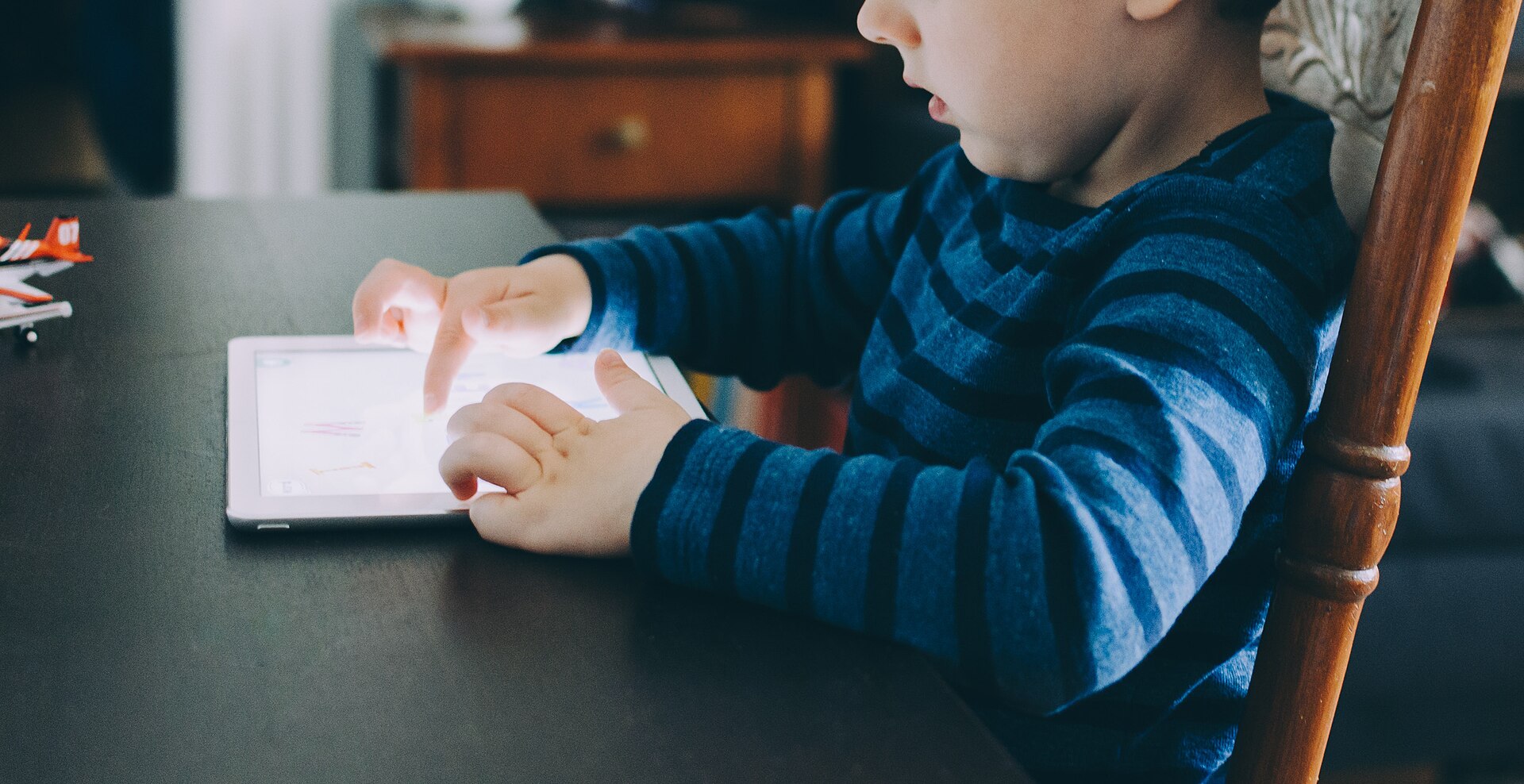 Young child playing a colourful game on a tablet at a dining table