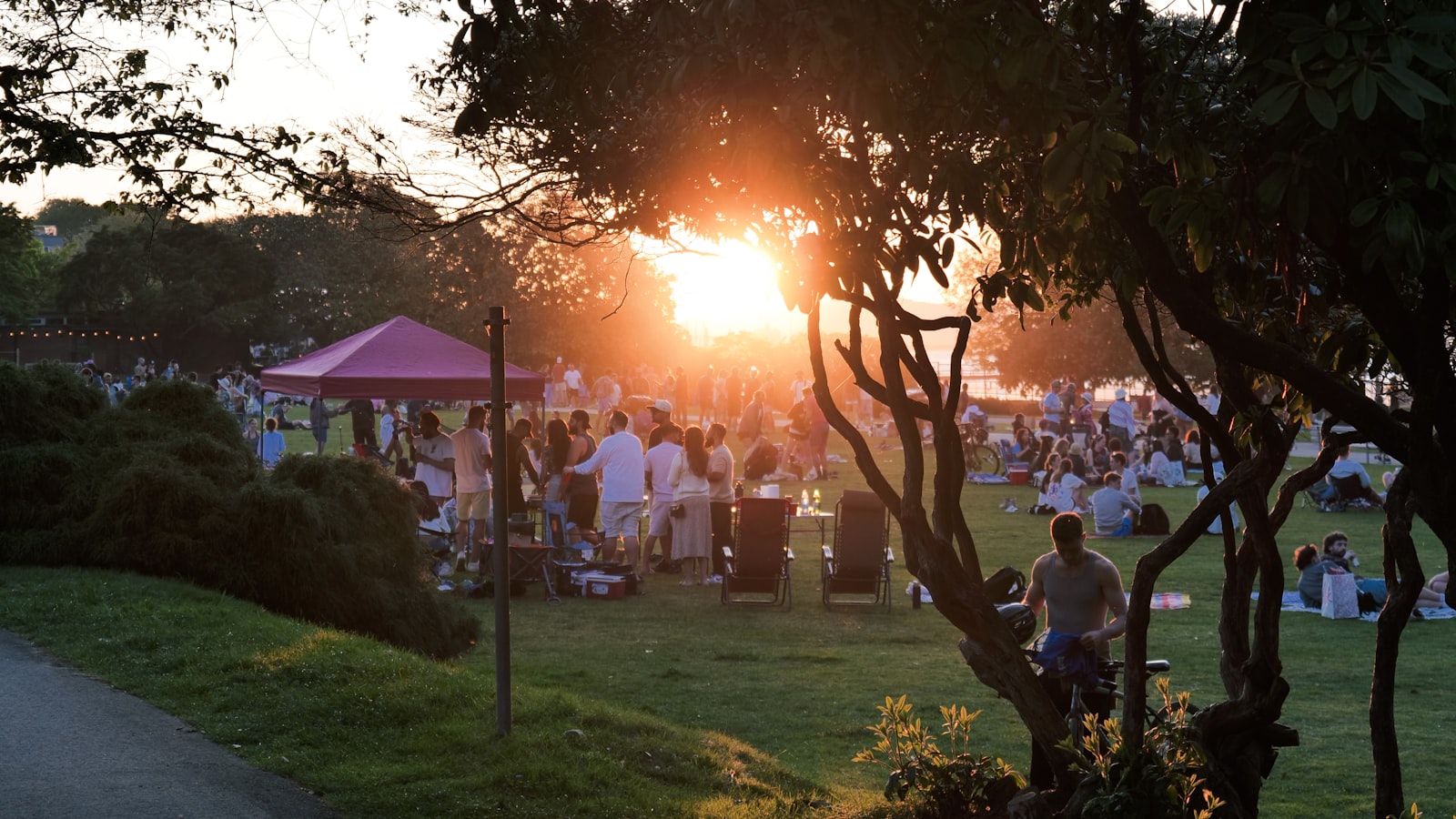 People gathered on the grass in a park at sunset before a free film screening