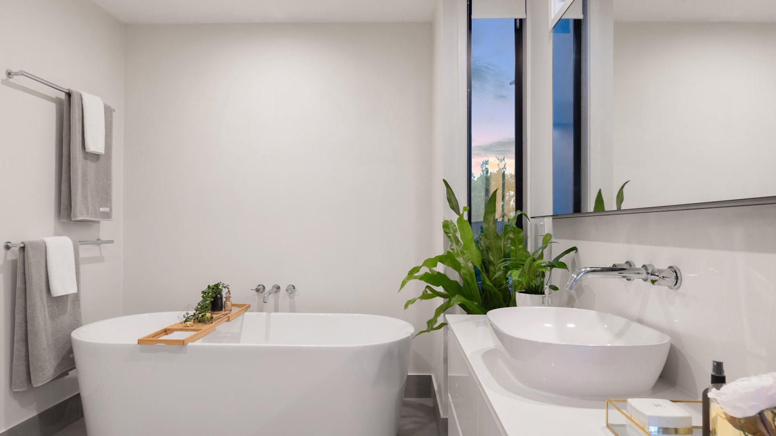 Small bathroom with wooden bath caddy tray, wall-mounted towel rails and basin storage