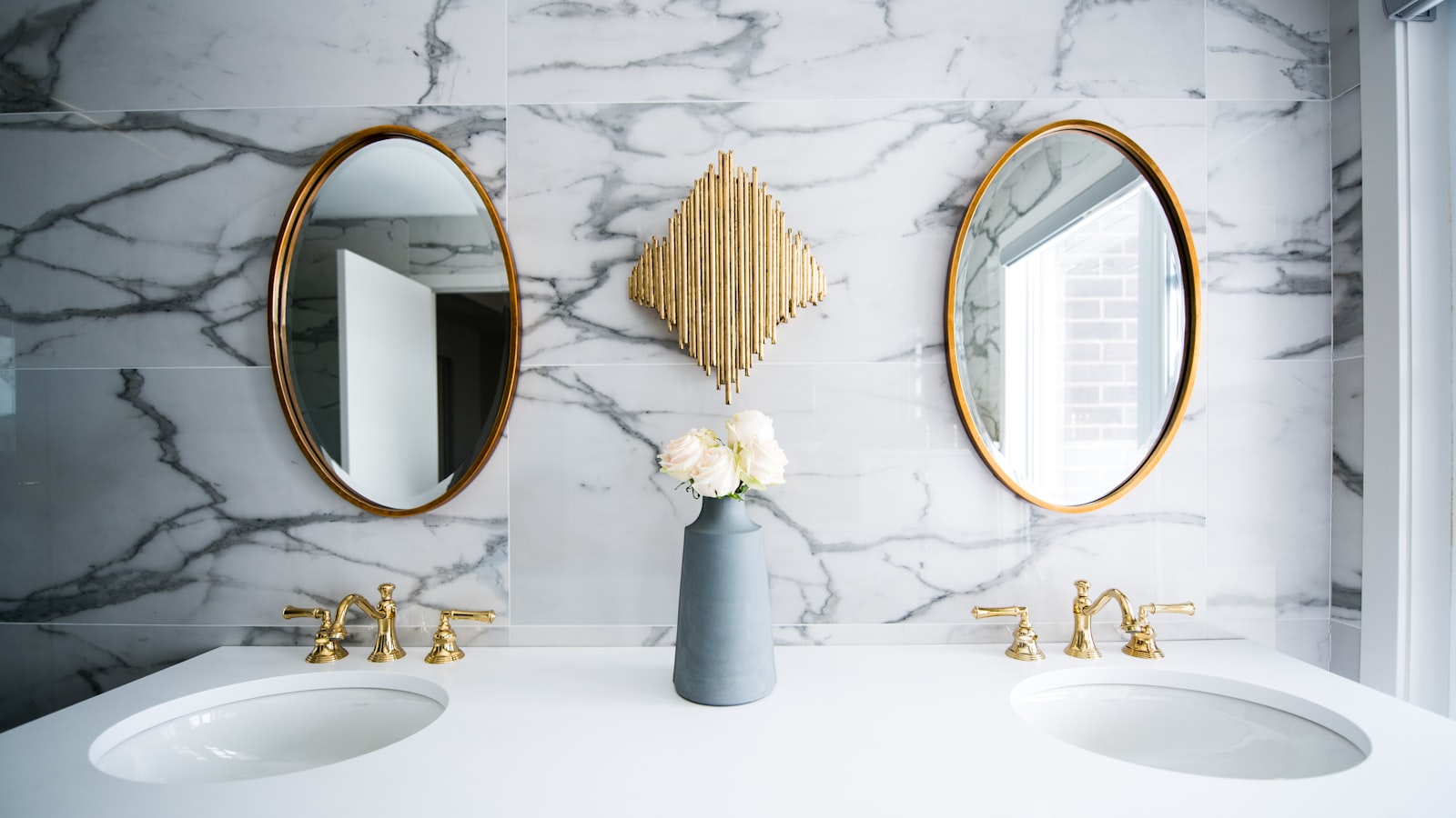 Double basin vanity with large oval mirrors - mirrored storage makes a small bathroom feel bigger