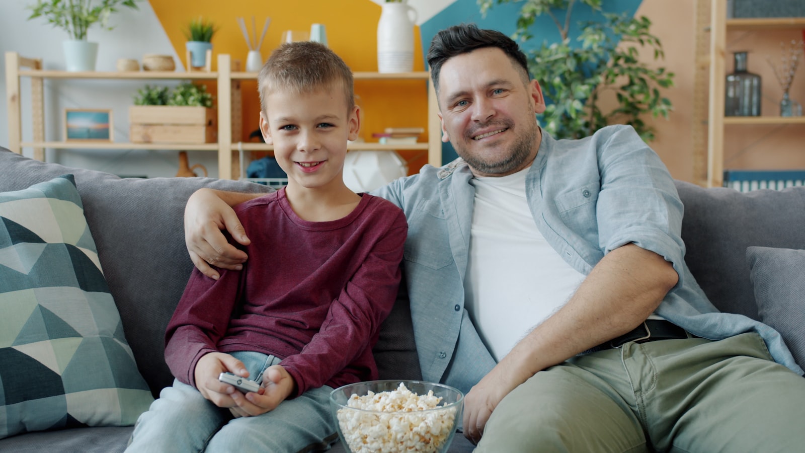 Father and son sharing popcorn on the sofa during a family TV night