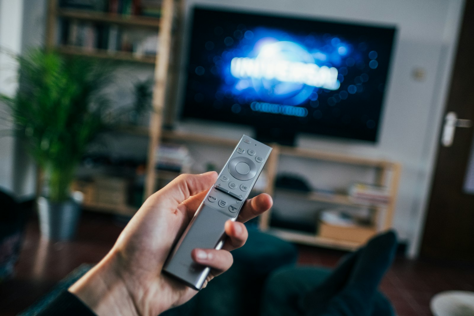 Hand holding a TV remote control in front of a screen