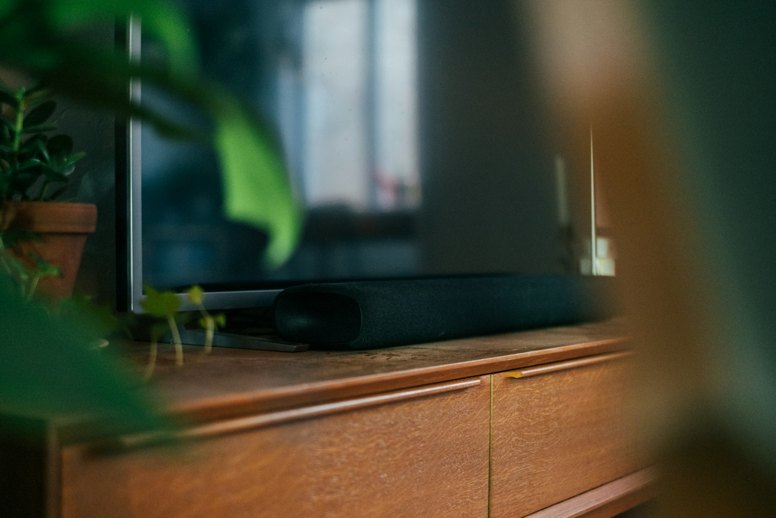 Slim soundbar sitting beneath a flat screen TV on a wooden media unit