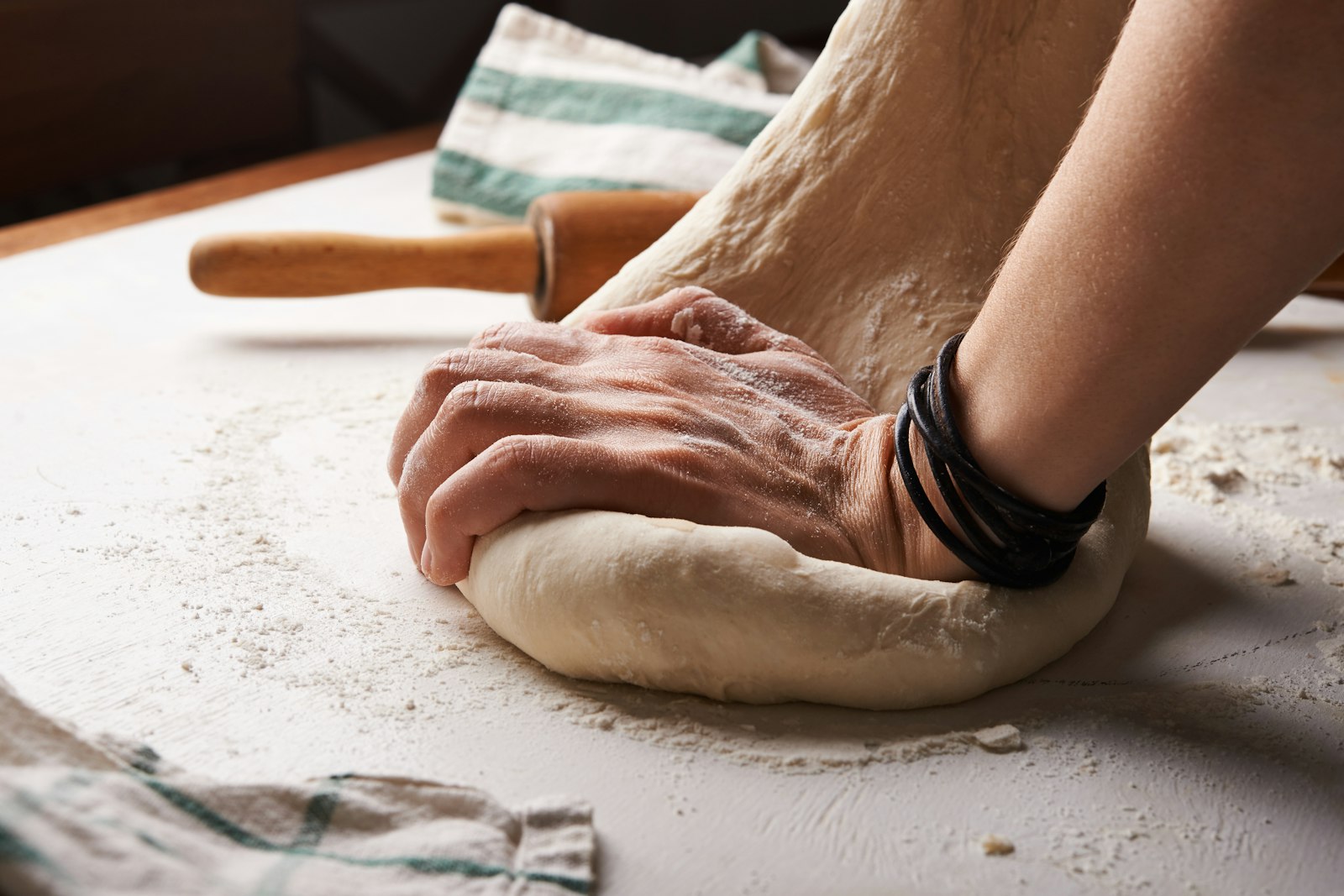 Hands kneading bread dough beside a wooden rolling pin