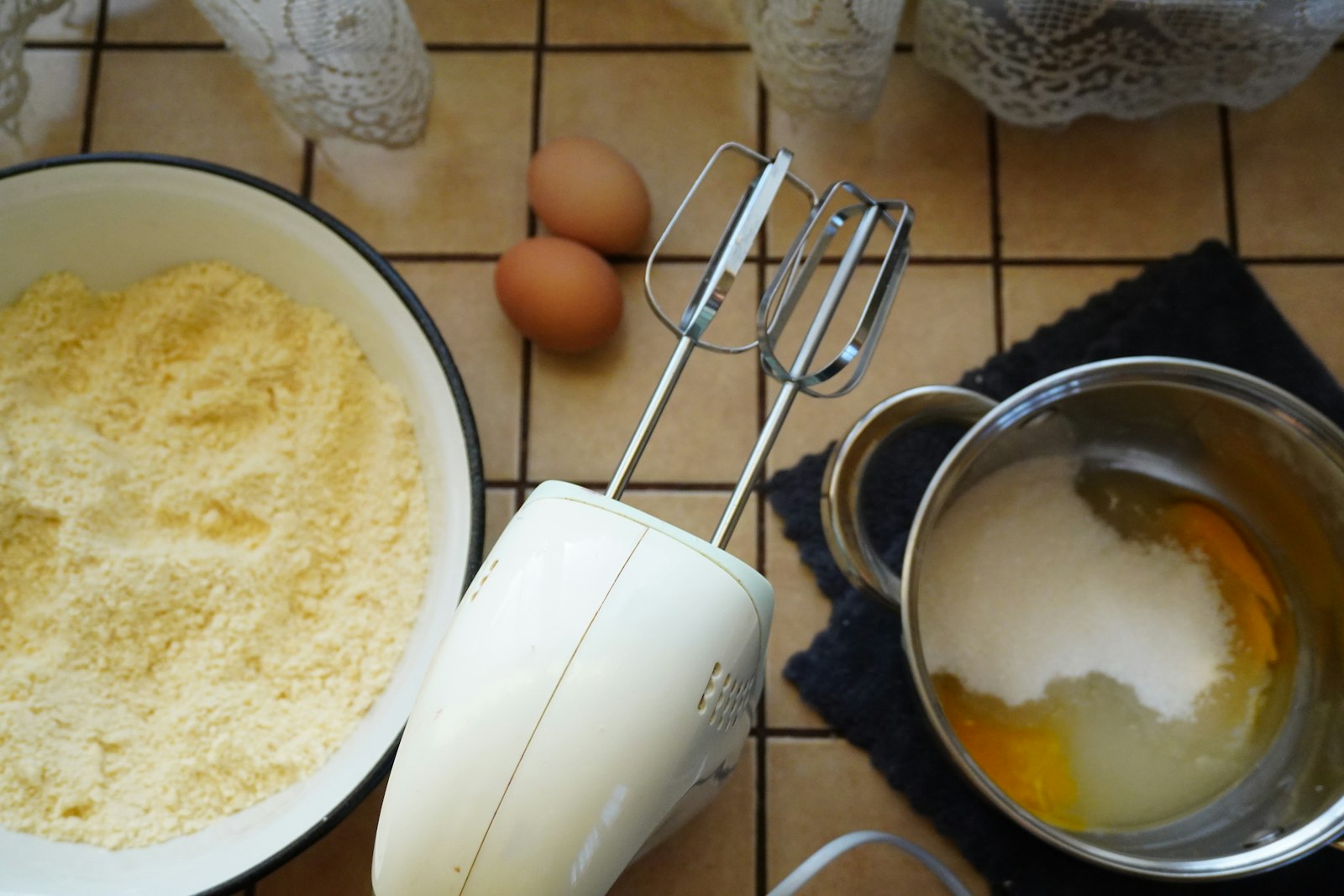Baking ingredients, eggs and an electric hand mixer laid out on a worktop