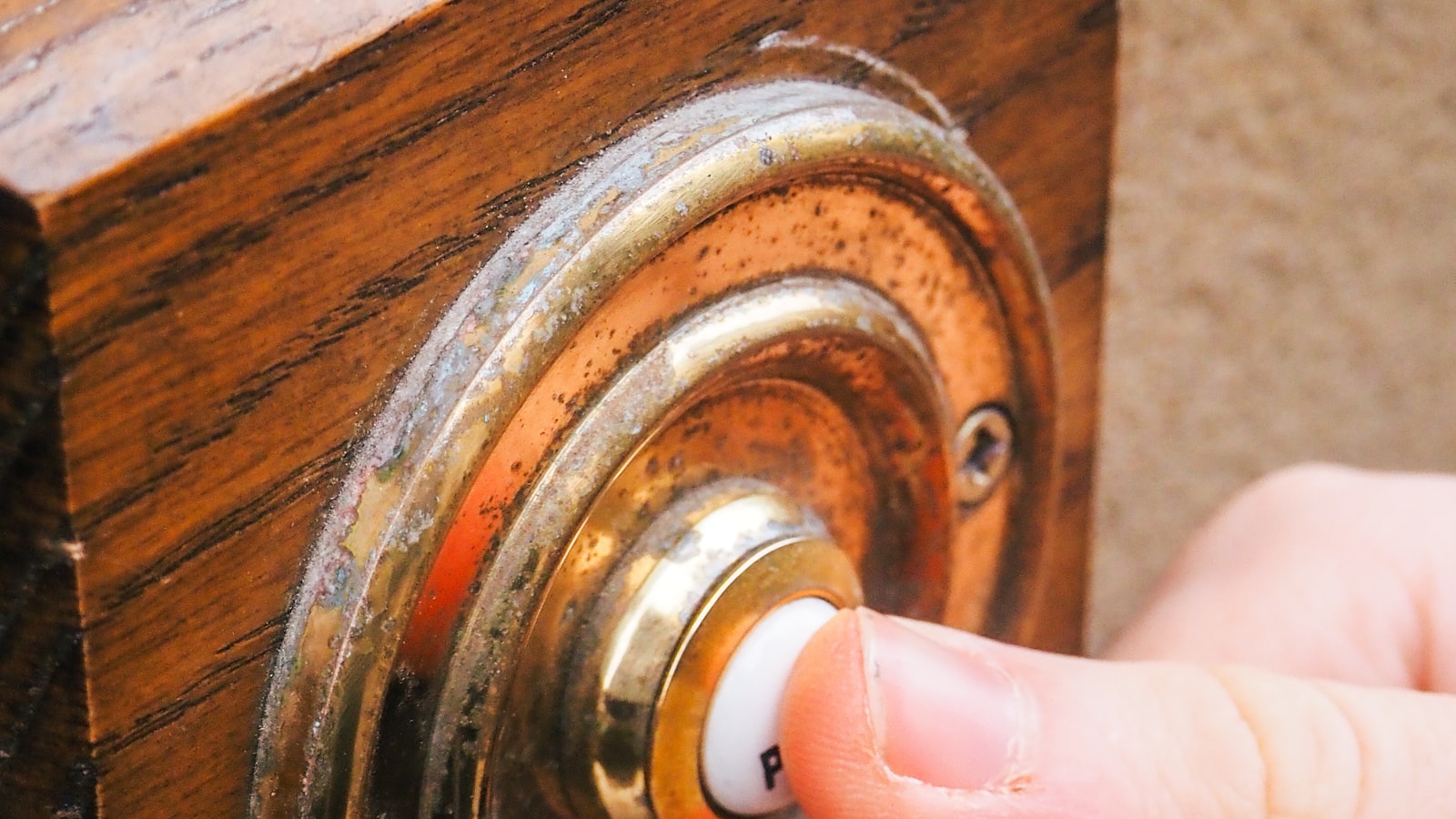 A hand pressing the button on a video doorbell fitted to a wooden front door