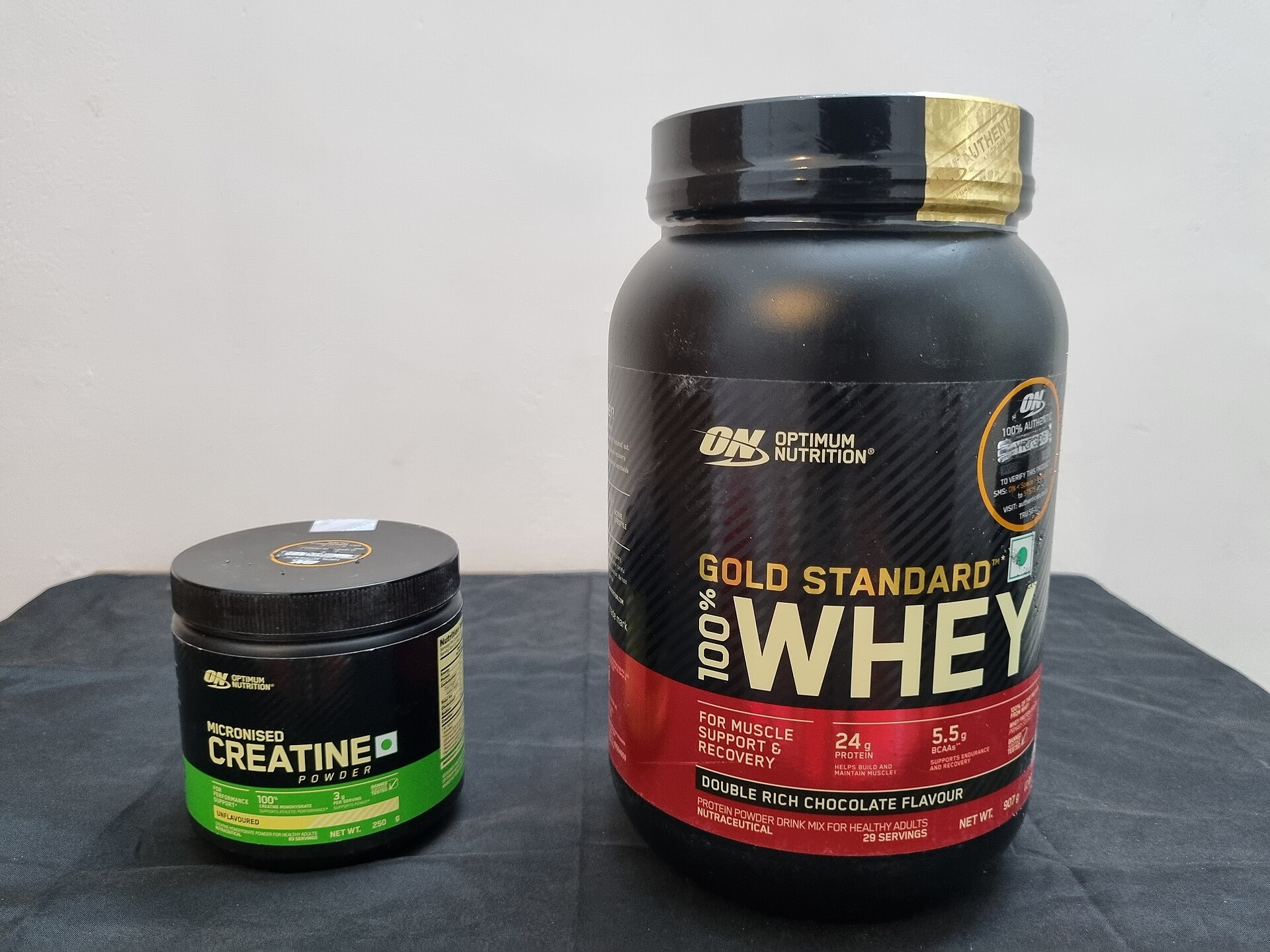 A large tub of whey protein next to a small tub of creatine powder