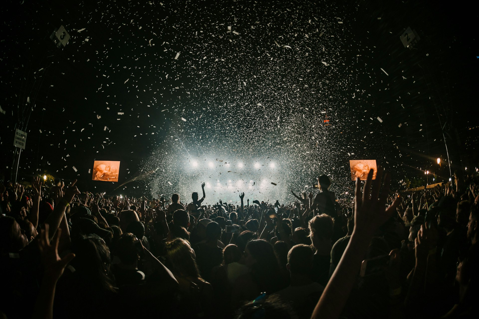 Confetti falling over a huge night-time festival crowd facing the main stage