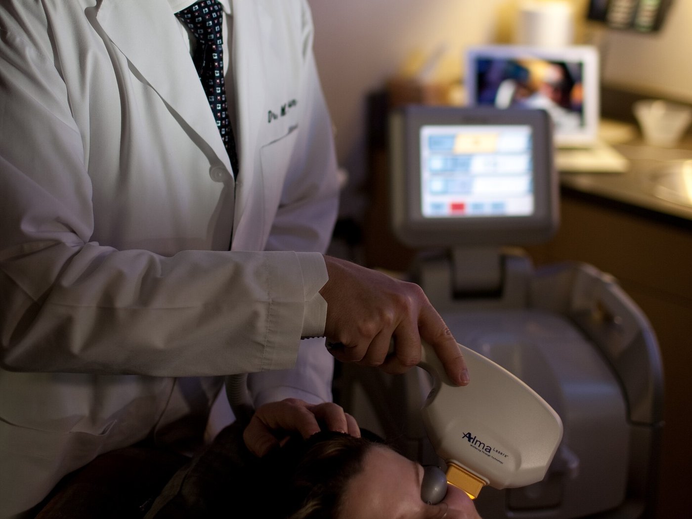 A clinician using a handheld light device on a patient's face - the dose-controlled setting where questions about whether LED face masks work get properly answered