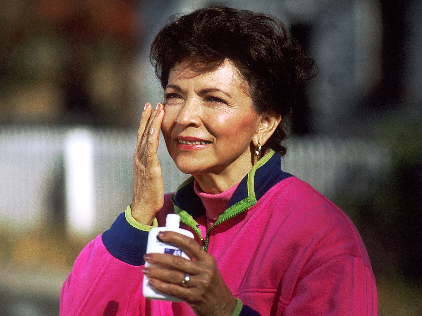 Woman applying sunscreen to her face outdoors - the unglamorous skincare step with the strongest evidence behind it
