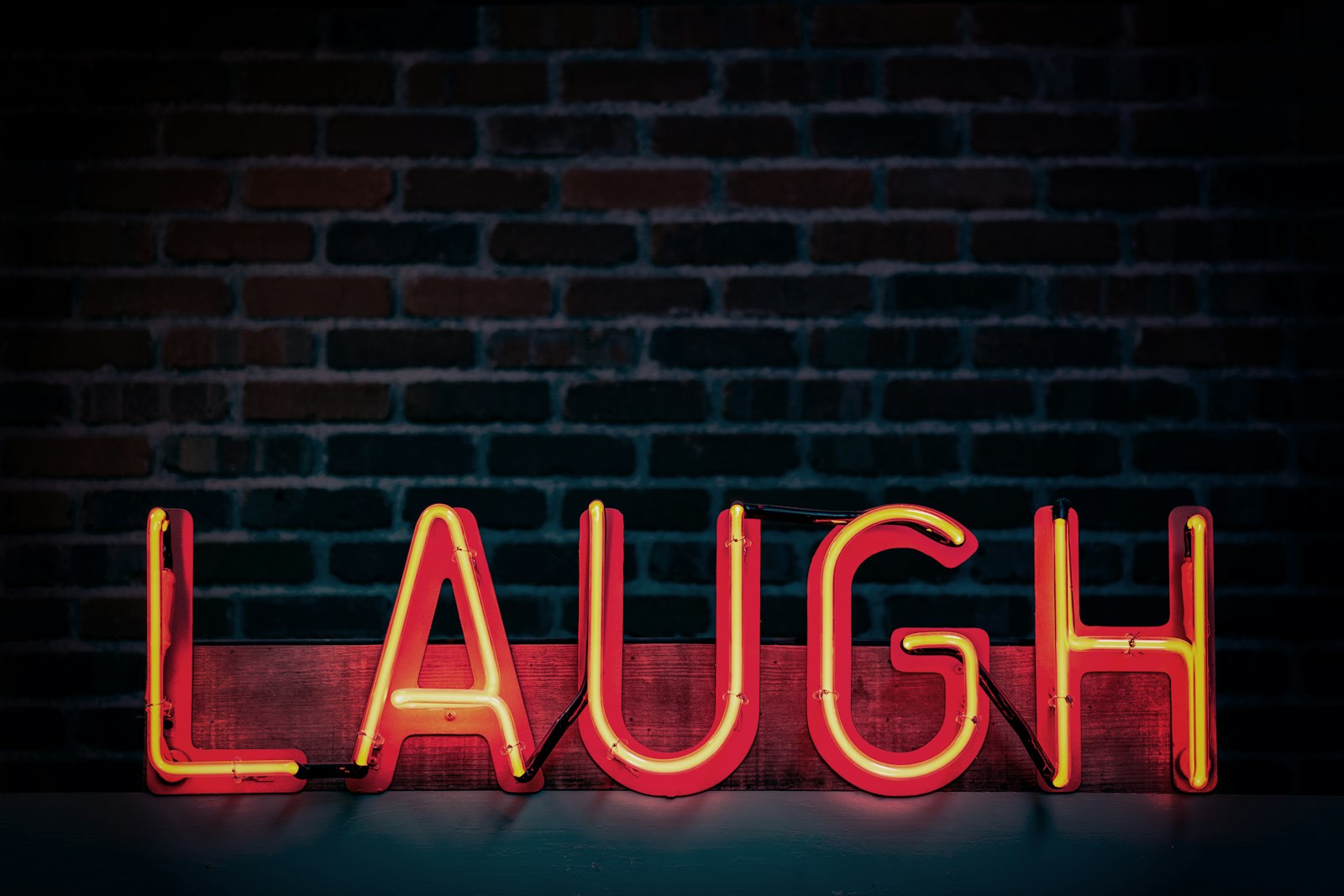 Red neon sign reading LAUGH against a brick wall
