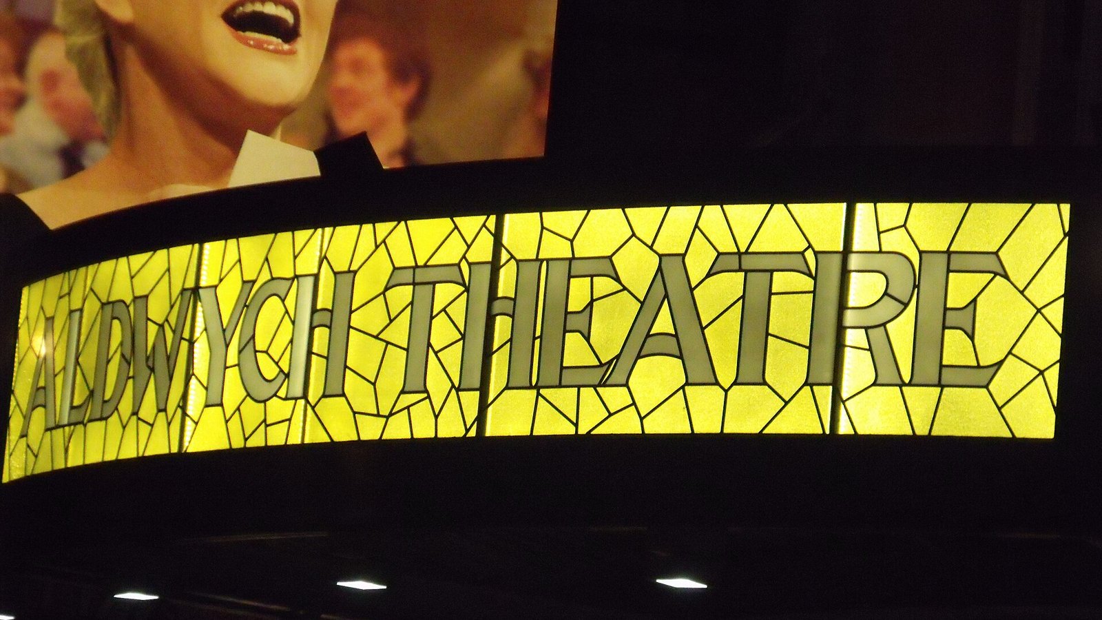 The illuminated yellow stained-glass Aldwych Theatre sign at night in London's West End
