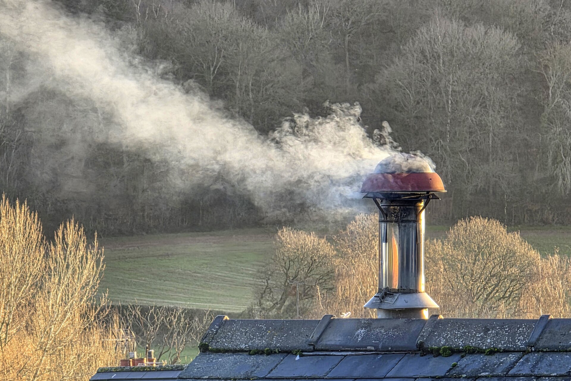 Smoke from a flue above a slate roof in the English countryside, illustrating the log burner rules in 2026