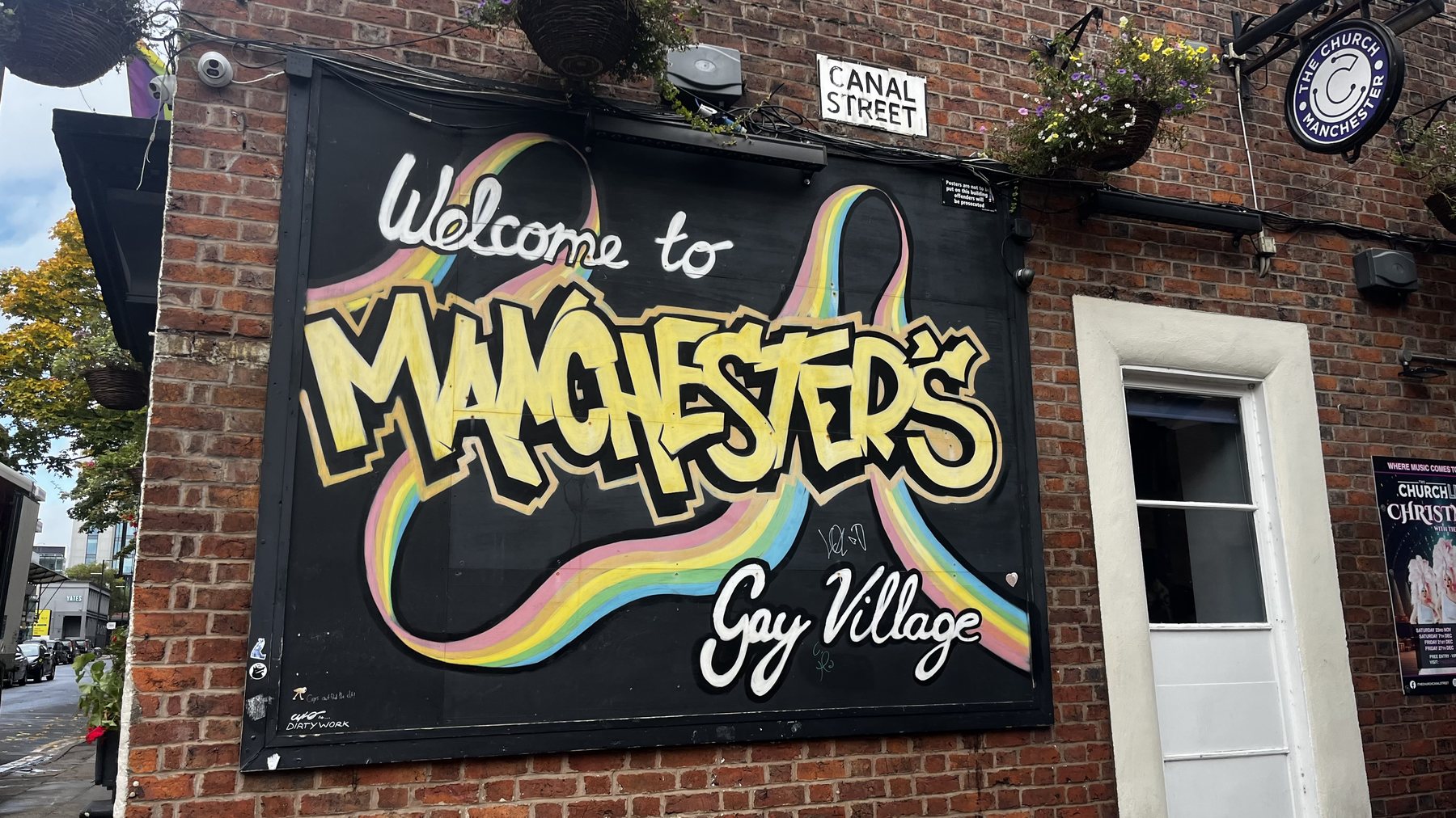 Welcome to Manchester's Gay Village mural beneath the Canal Street sign