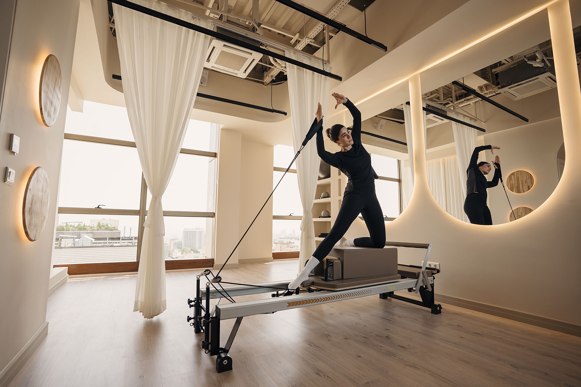 A reformer pilates class underway in a boutique studio, with a client mid-exercise on the machine