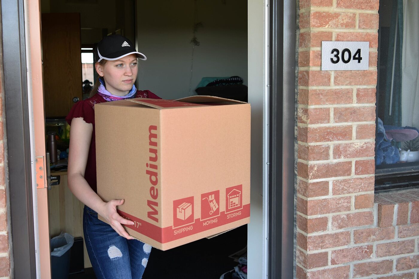 Student carrying a box of uni room essentials through a halls doorway on move-in day