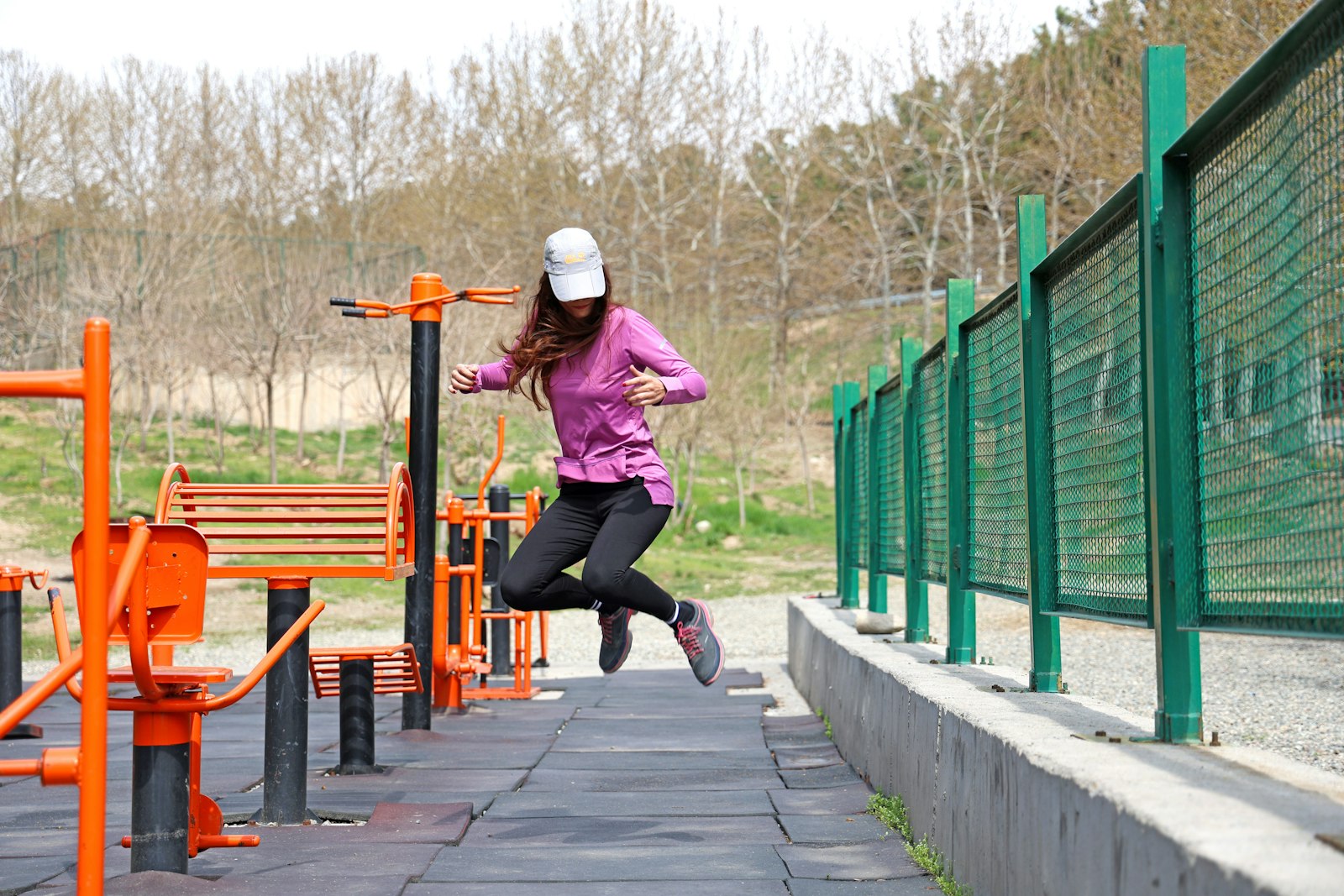 Woman mid-jump beside outdoor exercise equipment - impact, not walking, is what bone actually responds to