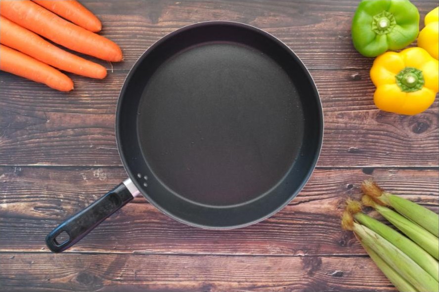 Fresh vegetables next to a frying pan on a wooden kitchen counter, illustrating everyday cooking with seed oils