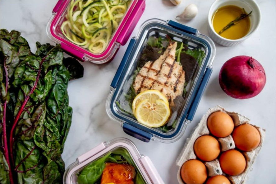 Meal prep containers with grilled chicken, vegetables and a small dish of olive oil dressing