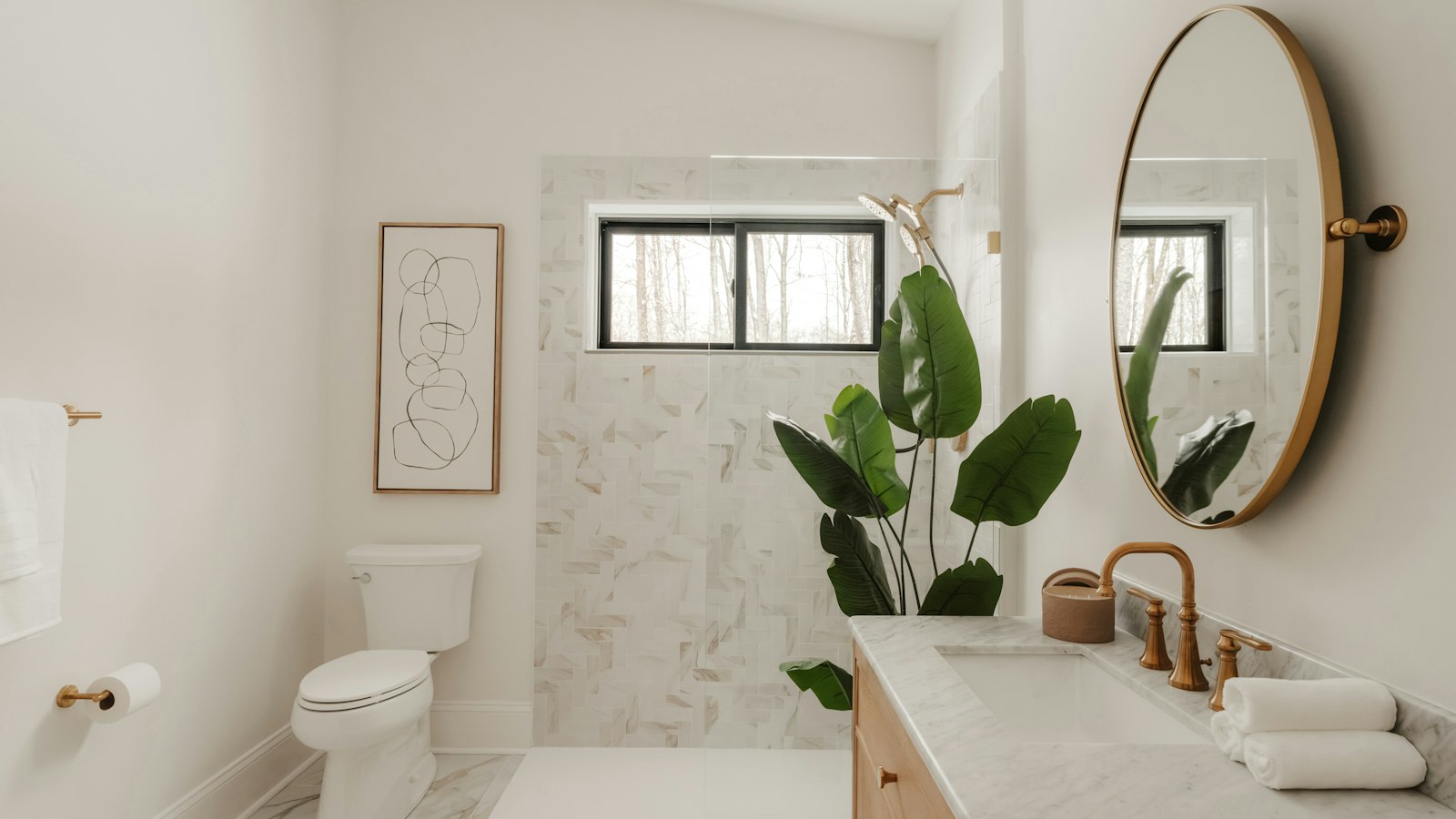 Brass basin taps, a round mirror and warm lighting in a modern bathroom