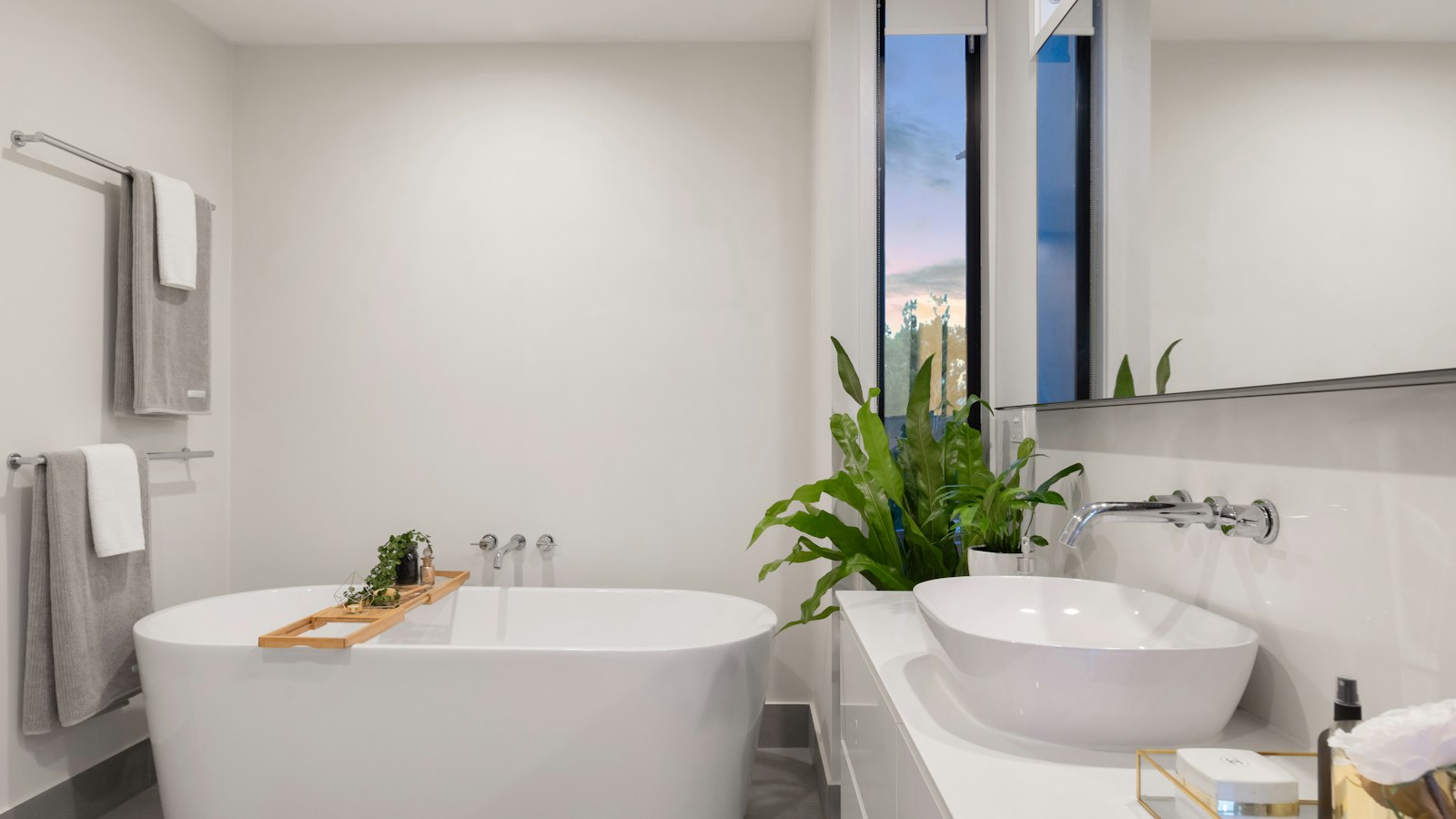 A white freestanding bath with a plant and timber bath tray