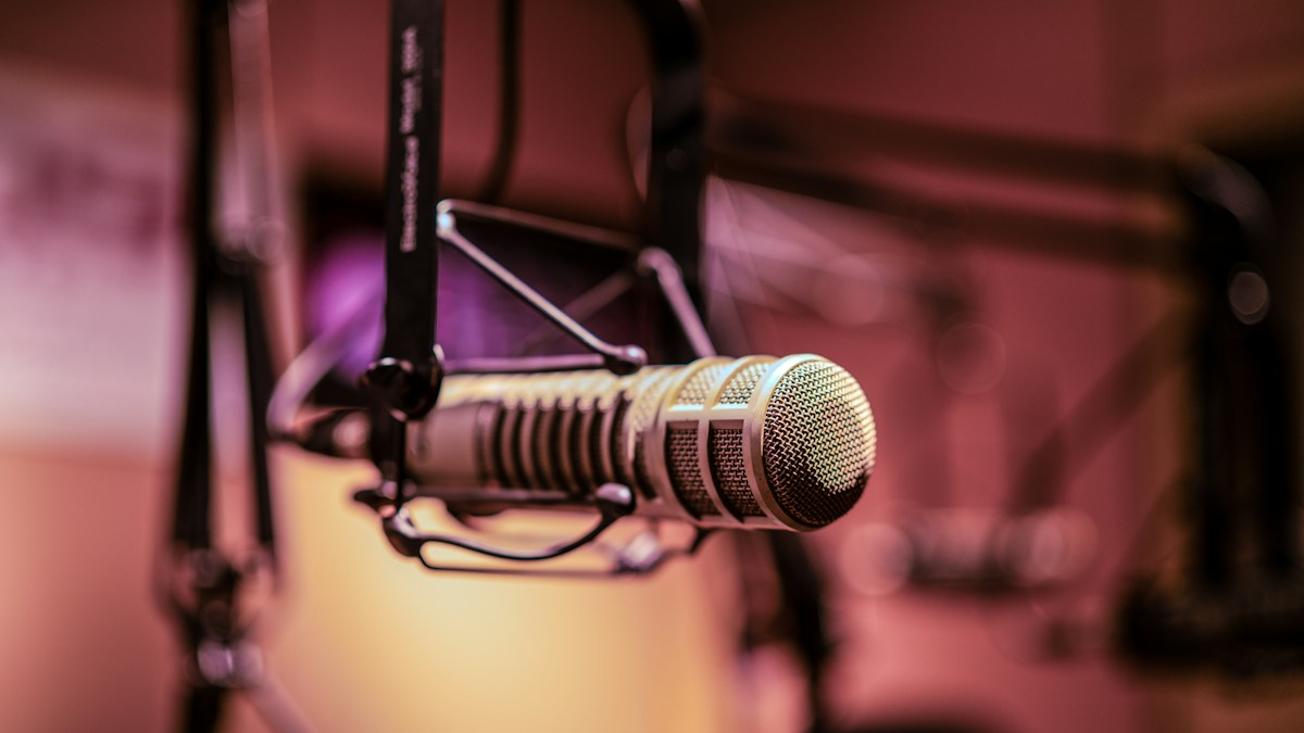 Studio microphone on a stand in a recording studio, lit against a dark background